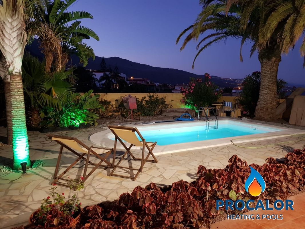 Piscina compacta con palmeras e iluminación al atardecer, instalada por PROCALOR