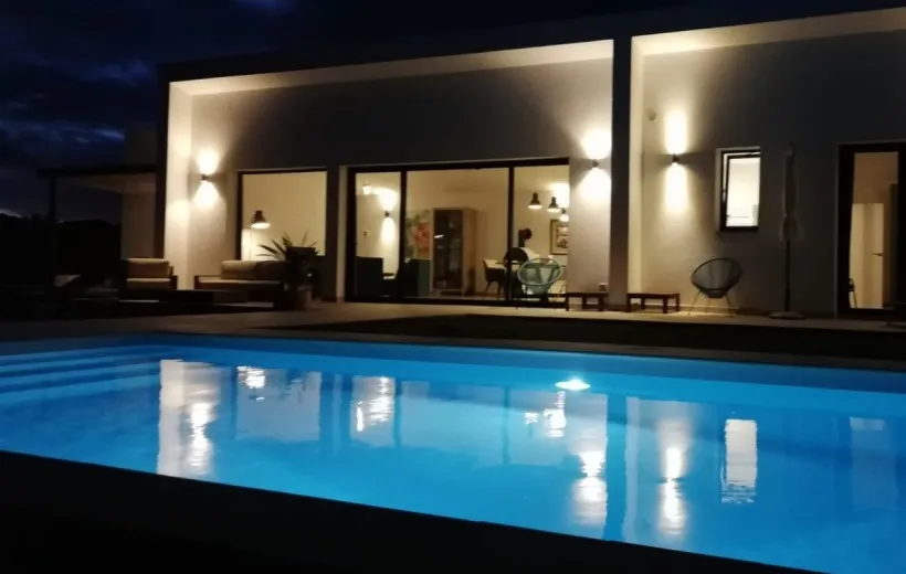 Piscina iluminada de noche con focos LED, frente a una casa